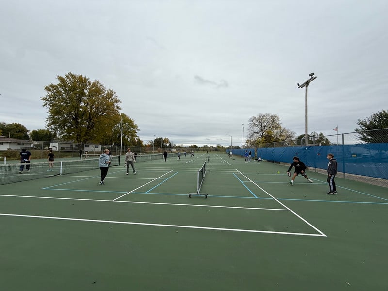 A physical education class plays pickleball on a tennis court.