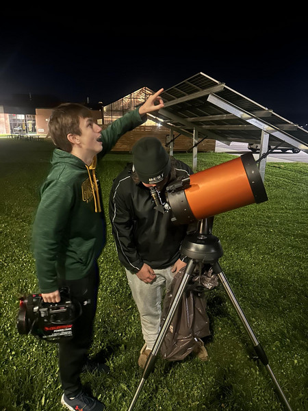 Two students are with a telescope, one point at the sky and one looking through it.