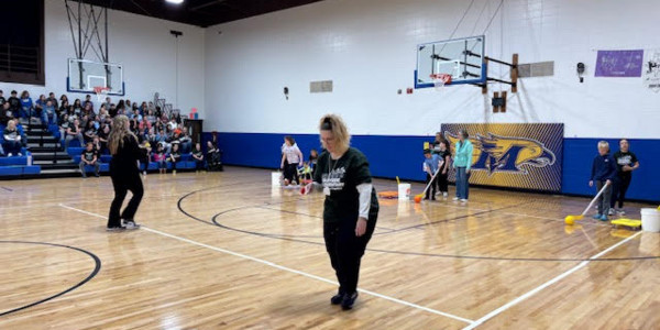 Students watch from the bleachers as staff prepare to participate in an activity in the gym.
