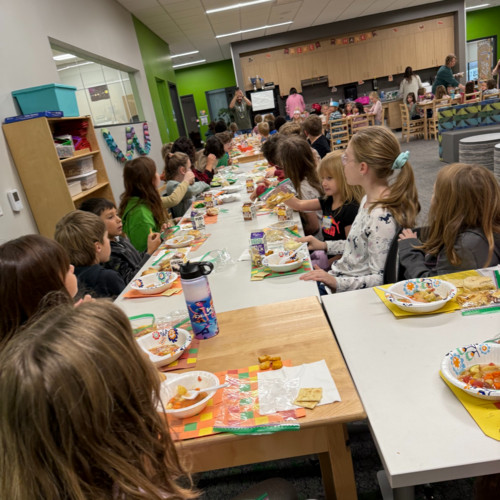 Elementary students sitting together at long tables eating a communal holiday or Thanksgiving meal.