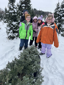 Students posing with a cut Christmas tree in a snowy field at Wagner Tree Farms.