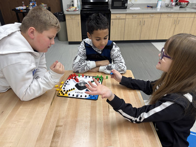 Students focused on a game of Trouble at a wooden table in a classroom makerspace.