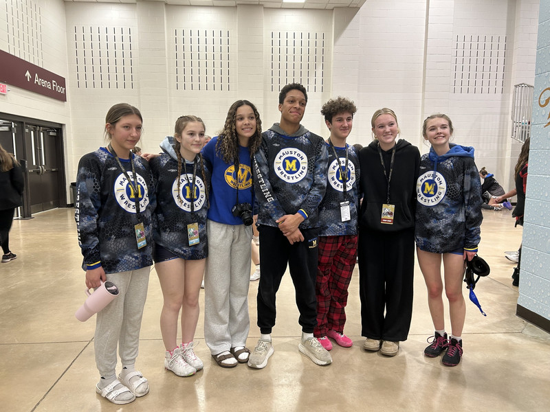 Seven student athletes from the Mauston Wrestling team pose together in an indoor arena hallway.