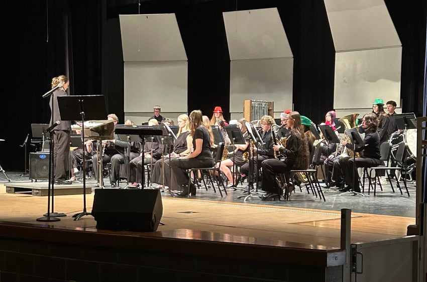 A student concert band performs on stage under the direction of a conductor.